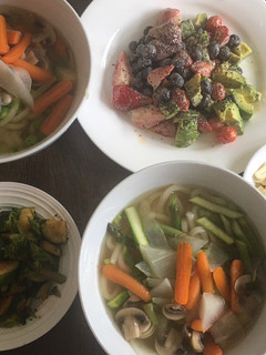 A picture of Udon noodle soup w/ side dishes of zucchini & fruit.