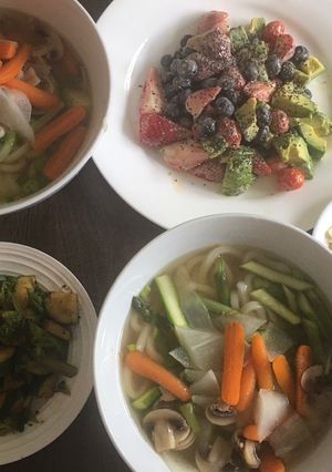 A picture of Udon noodle soup w/ side dishes of zucchini & fruit.
