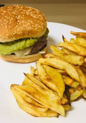 Una foto de Hamburguesa con guacamole, queso, cebolla y patatas fritas al horno