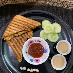 A picture of Chole bread sandwich with masala chai and cucumber.