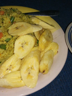 A picture of Fried rice, plantain with peppered meat.