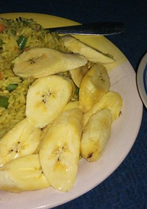 A picture of Fried rice, plantain with peppered meat.