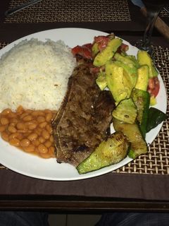 Una foto de Chuleta de res a las brasas, frijoles & puerco, ensalada de aguacate y zuchinni a la plancha