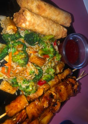A picture of Teriyaki chicken and pineapple skewers with fried rice and veggies and eggs rolls.