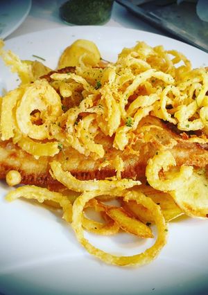 A picture of Fried European Sole on a Bed of Potatoes and Garlic with Onion Rings.
