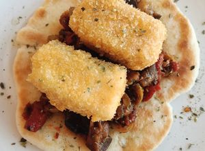 Una foto de Caponata siciliana con bacalao empanado sobre pan naan