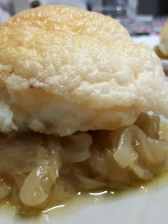 Una foto de Bacalao cubierto de muselina de ajo sobre cebolla caramelizada