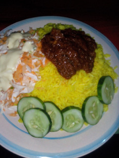 A picture of Curry Rice and stew, Garnished with cucumber and salad.