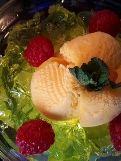 Una foto de Helado de mandarina con gelatina de limón al vodka, frambuesas y azahar con hierbabuena