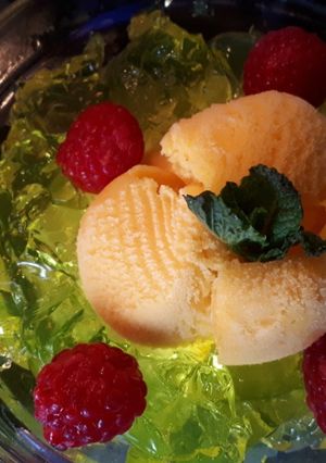 Una foto de Helado de mandarina con gelatina de limón al vodka, frambuesas y azahar con hierbabuena
