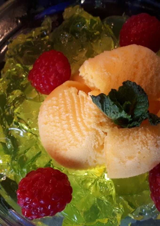 Una foto de Helado de mandarina con gelatina de limón al vodka, frambuesas y azahar con hierbabuena
