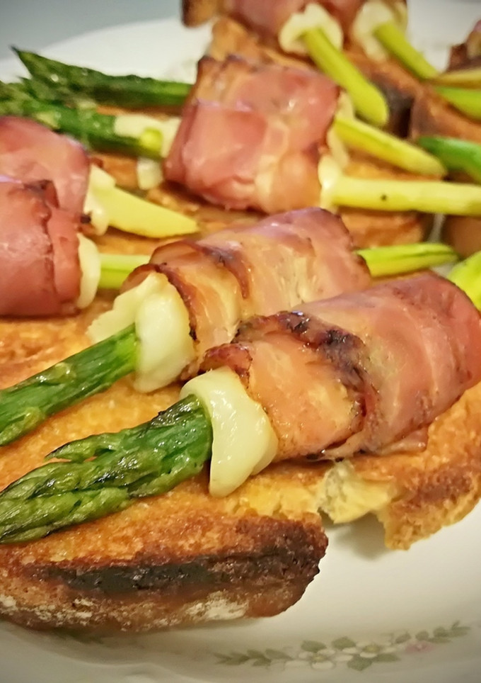 Una foto de Tostas con espárragos envueltos en bacon y queso fundido