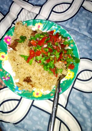 A picture of Boiled rice garnished with some onions,tomatoes and coriander.