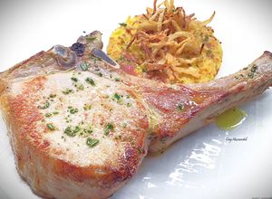 Foto di Braciola di maiale con manico, patate pasticciate e cipolla fritta