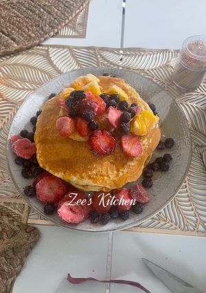 A picture of Pancakes with loads of fruits and honey.