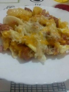 Una foto de Patatas con beicon, jamón york, salchichas y huevos rotos con queso y gratinado