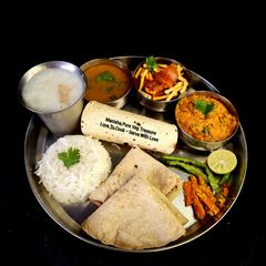 A picture of Kathiyawadi Lunch Thali (Dahi Tikhari, Sev Tameta Nu Shak, Dal Bhaat, Fulka Rotli, Chaas, Papad).
