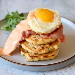 A picture of Corn cake with bacon and sriracha mayo sunny side up.
