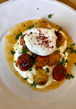 A picture of Hot charred cherry tomatoes with cold yoghurt and poached egg.