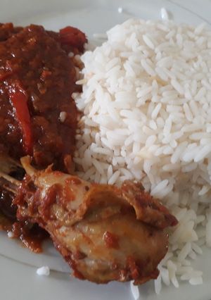 A picture of White rice with tomato stew and chicken.