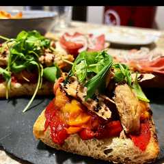 Una foto de Tosta de pimiento caramelizado, tomate confitado, melva y rúcula