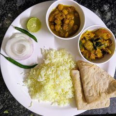 A picture of Veg lunch thali with rice, chhole, mushroom masala and chapati.