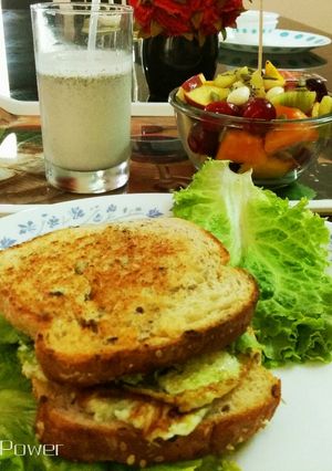 A picture of Egg sandwich with fruit salad and almond pumpkin seeds milkshake.