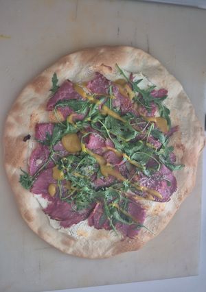 Una foto de Pizza blanca de pastrami y rúcula