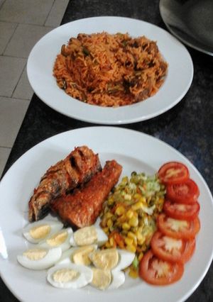 A picture of Jollof Rice peppered glazed fish and corn veggies.