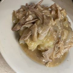 A picture of Shredded chicken and gravy over mashed potatoes.