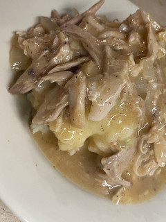 A picture of Shredded chicken and gravy over mashed potatoes.