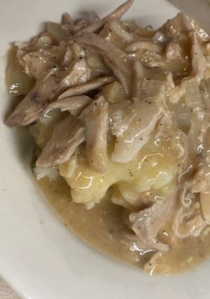 A picture of Shredded chicken and gravy over mashed potatoes.