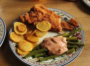 Una foto de Pescado frito en milanesa, tomate con ajo, espárragos, papas fritas