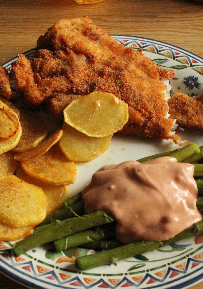 Una foto de Pescado frito en milanesa, tomate con ajo, espárragos, papas fritas