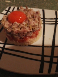 Una foto de Tartar ibérico con tomates y yema curada sobre cama de couscous