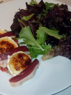 Una foto de Ensalada de brotes tiernos y rulo de queso de cabra caramelizado, jamón de pato, y vinagreta de mango y fresa