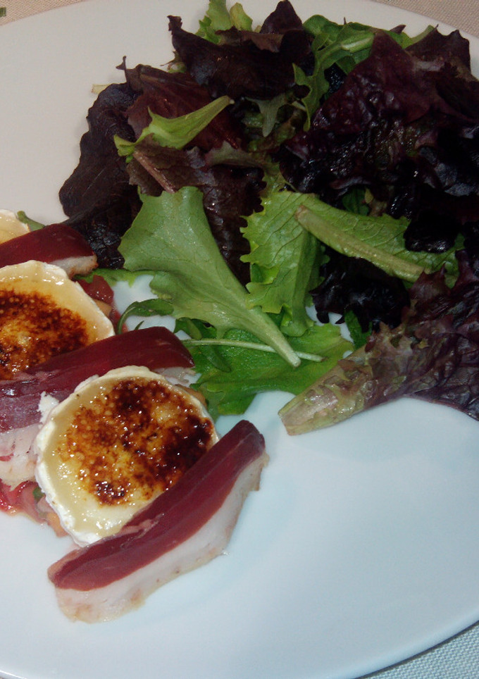 Una foto de Ensalada de brotes tiernos y rulo de queso de cabra caramelizado, jamón de pato, y  vinagreta de mango y fresa
