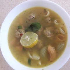 A picture of Meatball soup with pasta and herbs.