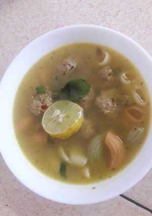 A picture of Meatball soup with pasta and herbs.
