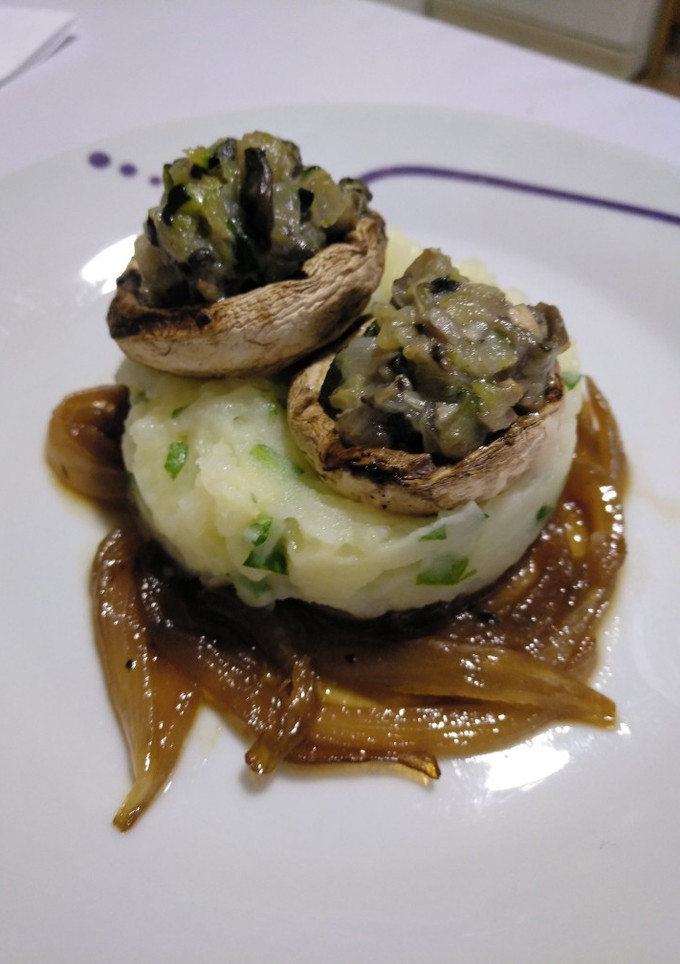 Una foto de Champiñones rellenos sobre puré de patatas en cama de cebolla