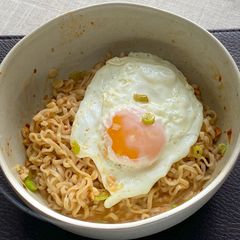 A picture of Jah Jan Mien (instant packet noodles) with peanut butter, spring onions topped with fried egg.