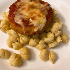 A picture of Parmesan chicken over macaroni and cheese.