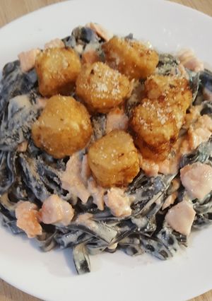 Une photo de Tagliatelles à l'encre de seiche, noix Saint Jacques avec sauce saumonée