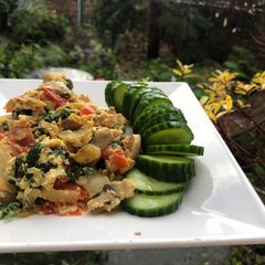 A picture of Scrambled eggs, parsley and tomatoes.