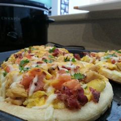 A picture of Breakfast pizza topped with eggs, chicken,applewood bacon, carme.