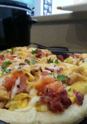 A picture of Breakfast pizza topped with eggs, chicken,applewood bacon, carme.