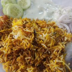A picture of Chicken briyani with raita and salad.