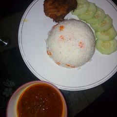 A picture of White rice and stew garnished with carrots and cucumber.