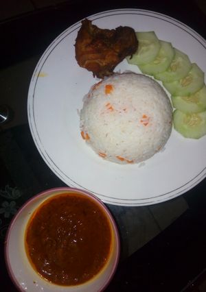 A picture of White rice and stew garnished with carrots and cucumber.