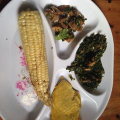 A picture of Boiled maize served with boiled sweet potatoes and fried beef with kales.